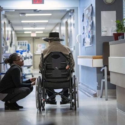 Staff speaking with patient in hospital hallway.