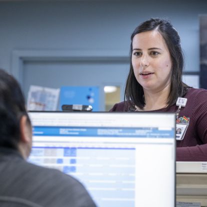 Paola standing by a counter, speaking to a staff member on a computer