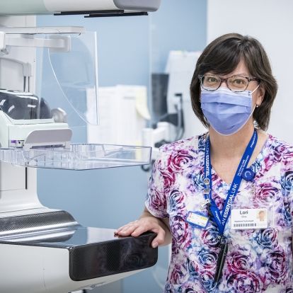 Lori Silva has short, dark hair and has glasses. She's pictured standing next to a piece of equipment at Breast Imaging Kingston.