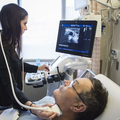 A healthcare practitioner using an ultrasound machine on a patients neck.