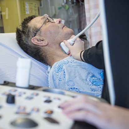 A healthcare practitioner using an ultrasound machine on a patients neck.