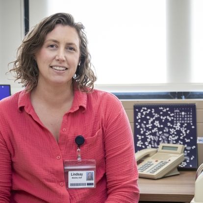 Lindsay MacDougall is pictured inside the Well Newborn and Parent Clinic, located at Kingston General Hospital. She has short, medium brown, wavy hair and blue eyes. She's wearing a bright pink, button down blouse.