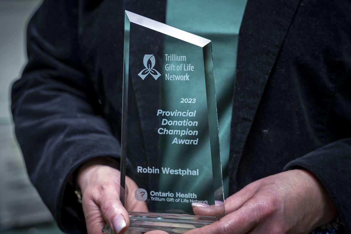 This is a close up shot of the 2023 Provincial Donor Champion Award, being held in Robin Westphal’s hands. The award is made of glass. Etched on it is 2023 Provincial Donor Champion Award, Ontario Health Trillium Gift of Life Network and Robin Westphal.