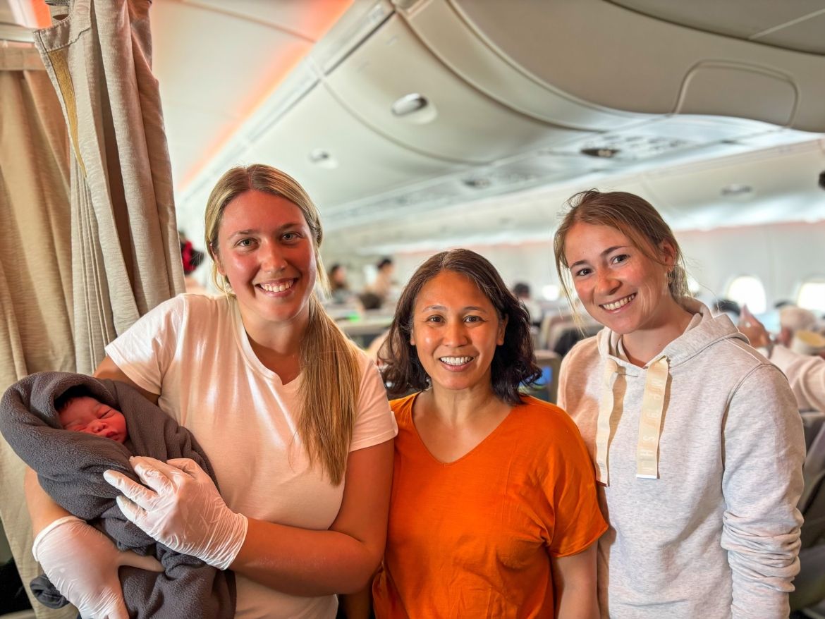 Three medical professionals holding a newborn baby on a plane