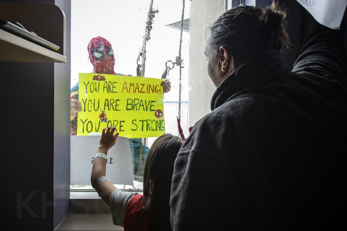 spiderman holds a sign up to a child in the hospital