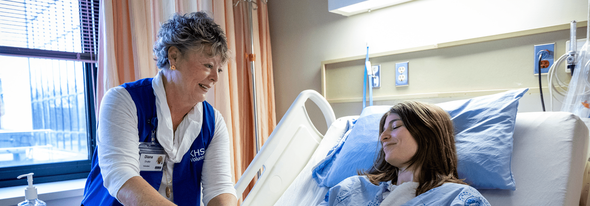 A volunteer is handing a patient a snack at the bedside.