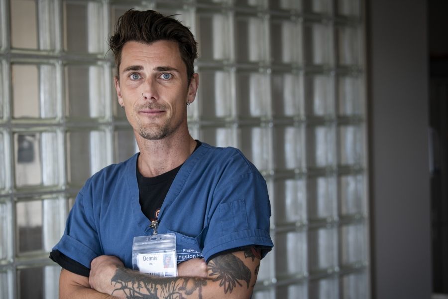 Dennis Clark is pictured standing outside the NICU at the KGH site. He has short brown hair, blue eyes and has tattoos on both arms. He’s wearing blue scrubs.