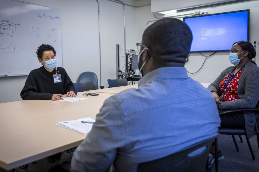 Members of the Black Staff Community Group are seated around a boardroom table as they meet. There are two Black women and one Black man. All have papers in front of them.