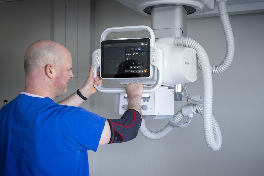 A person wearing blue scrubs positions a new x ray machine in a clinic room.