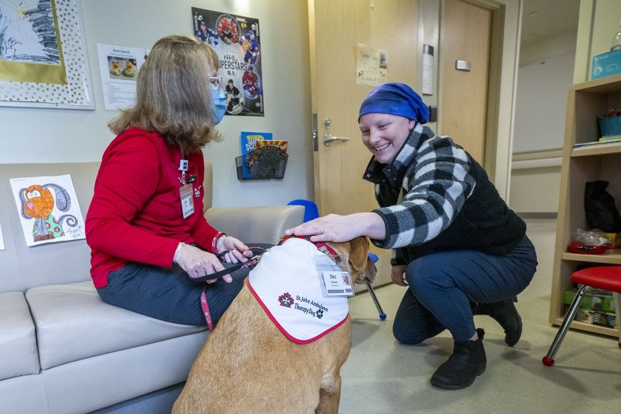 Julie Halle and Dog interact with a KHSC patient. The patient is crouching as she pets doc smiling. Julie is facing the patient and chatting.
