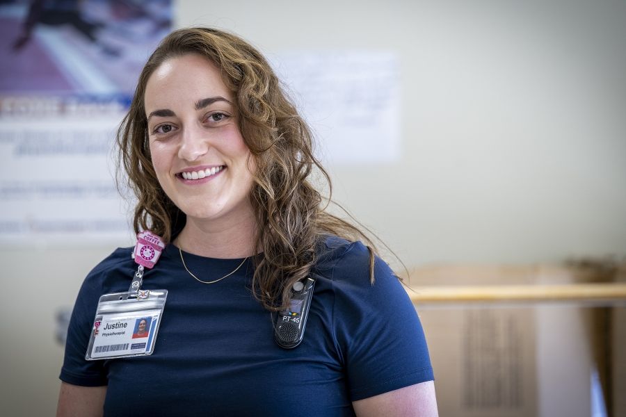 Justine White is photographed smiling directly into the camera. She has shoulder length, medium brown, wavy hair and brown eyes. She’s wearing a navy blue shirt with her KHSC ID badge.