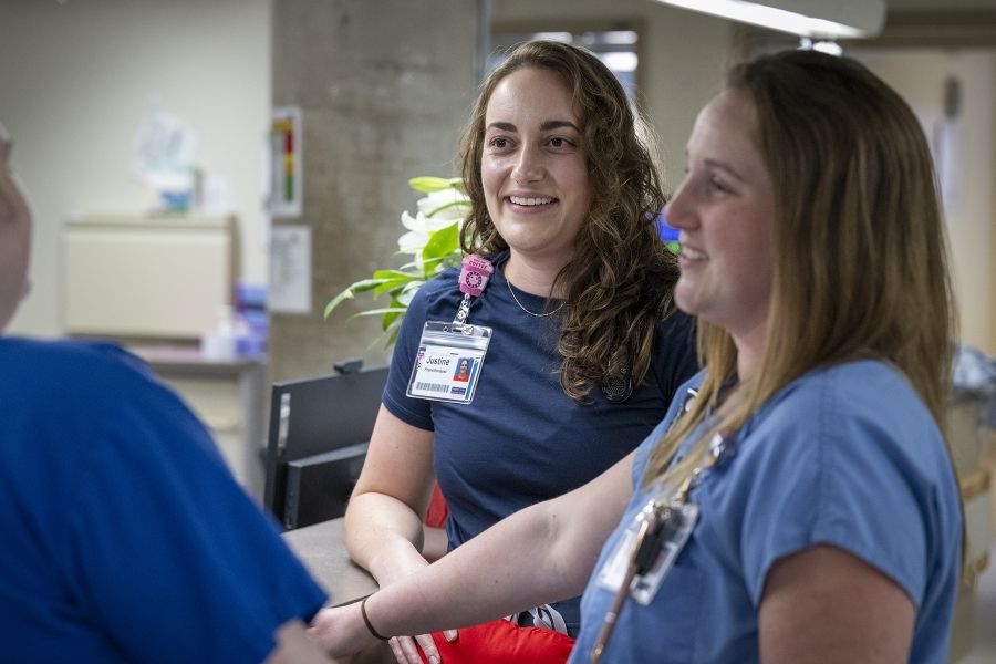 Justine White is standing next to physiotherapy assistant Danielle Knapton near a care desk. The duo are seen chatting and smiling with another person whose back is to the camera.