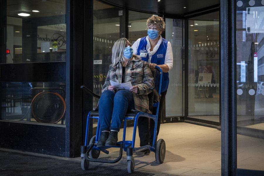 A volunteer is pushing a patient in a wheelchair outside the doors of Hotel Dieu Hospital.