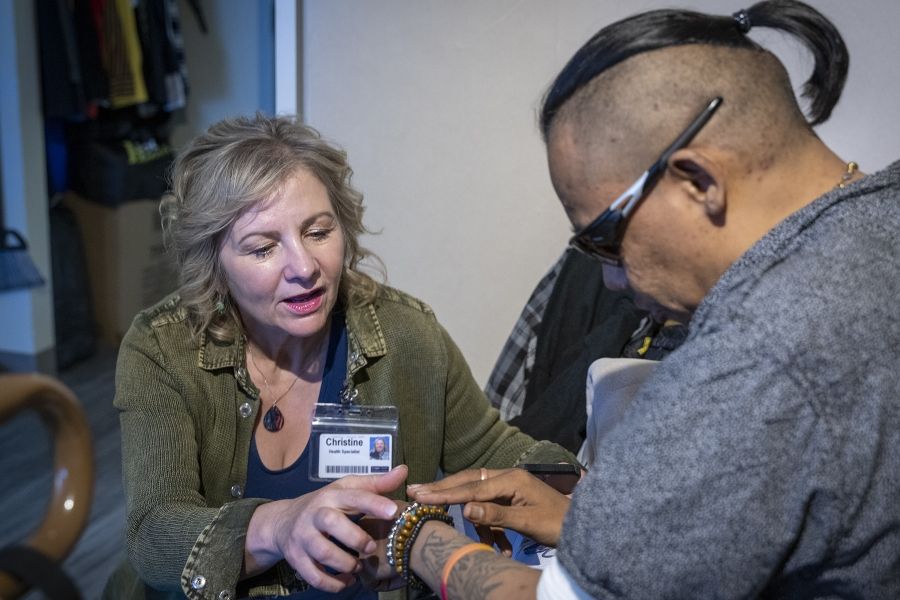 Christine Hennigar is crouched down while a guest sits across from her. She’s looking down at the guest’s wrist, which has traditional beaded bracelets.