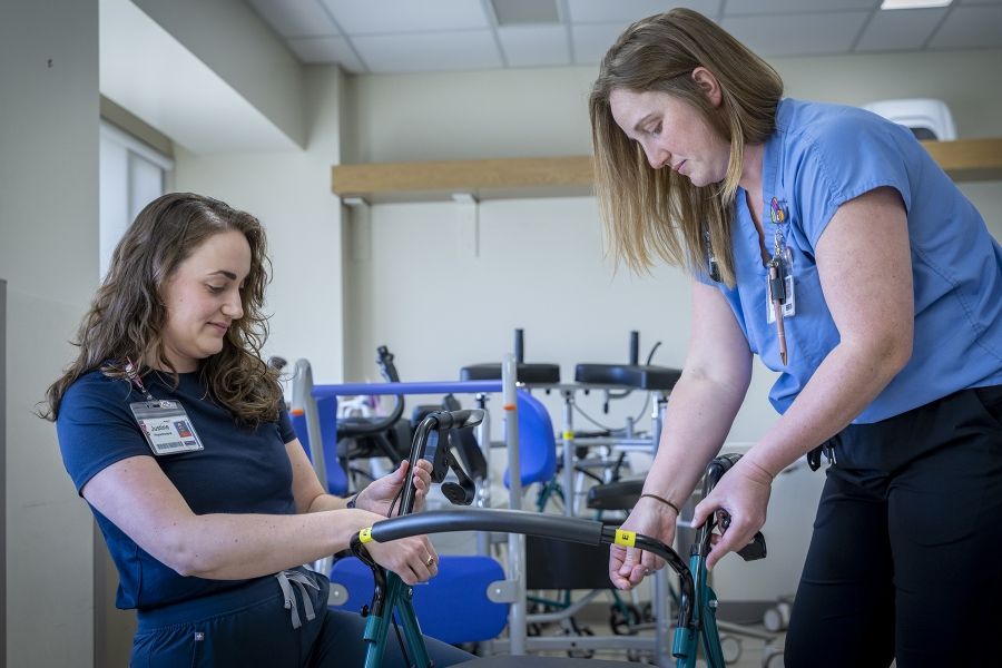 Justine White and physiotherapy assistant Danielle Knapton are putting together a walker, a mobility aid device. White has shoulder length, medium brown, wavy hair and brown eyes. She’s wearing a navy blue shirt with her KHSC ID badge. Knapton has straight medium brown hair and blue eyes. She’s wearing light blue scrubs with her KHSC ID badge.