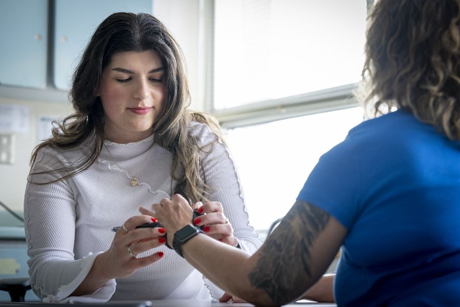 Andreea Bocicariu is sitting at a table in the Orthopedics and Plastics Clinic, across from a patient whose back is to the camera. She’s looking down at her patient’s hand, while wrapping a splint on it.