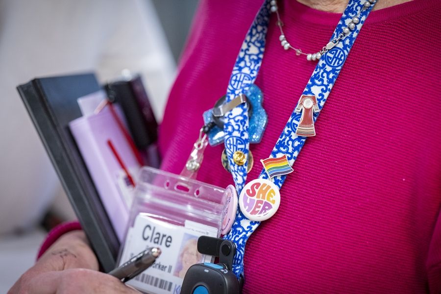 A close up shot of Clare Bowley’s decorated blue patterned lanyard, which features her KHSC ID badge and a number of pins like the Pride flag.