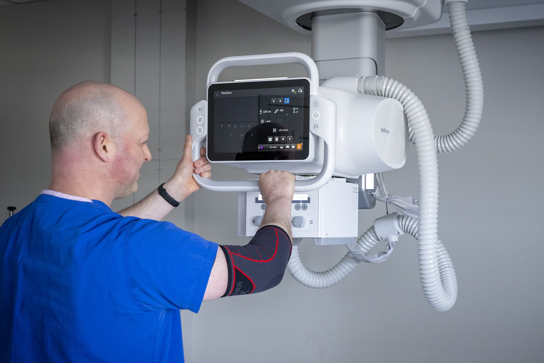 A person wearing blue scrubs positions a new x ray machine in a clinic room. 