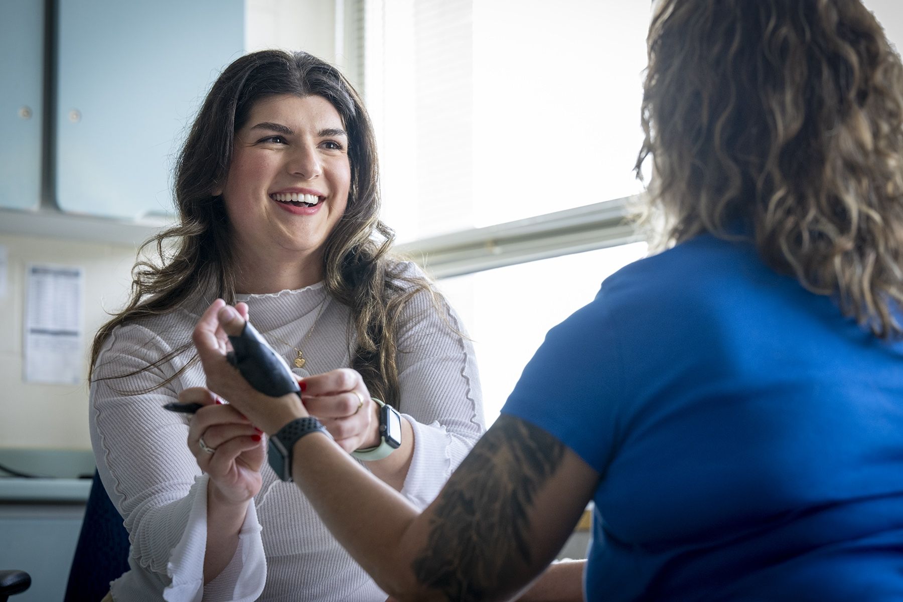 Andreea Bocicariu is sitting at a table in the Orthopedics and Plastics Clinic, across from a patient whose back is to the camera. She’s smiling from ear to ear at her patient, while wrapping a splint on her hand.