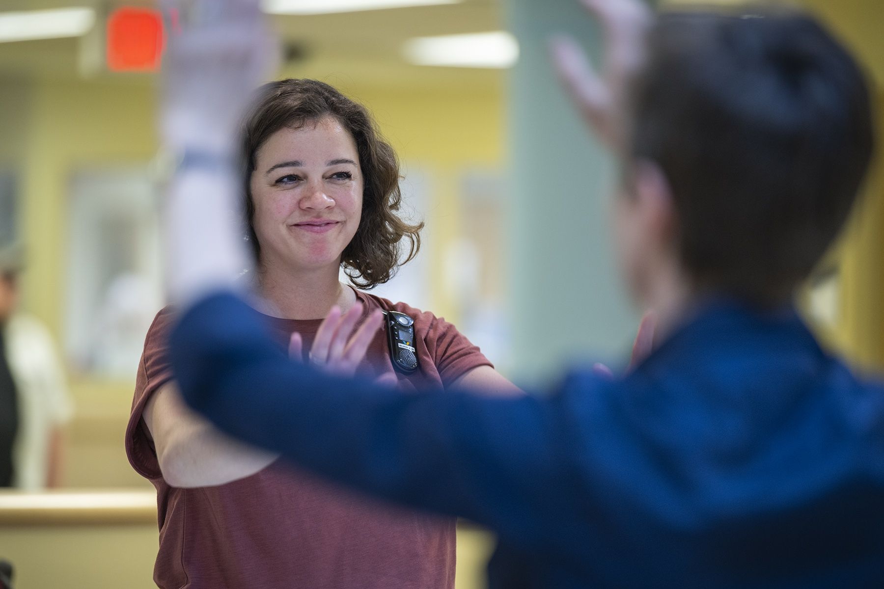 Laurie Hill is photographed leading her mindful movement group. Hill is standing with her arms out and smiling. She has short brown wavy hair and is wearing a dusty rose blouse and black pants.